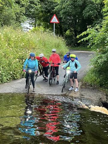 Cyclists trying to cross a river ford.