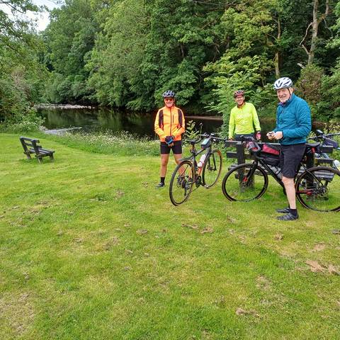 Cyclists posing on grass beside River Stinchar.