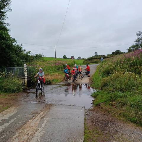 Several cyclists attempting to cross small river ford.