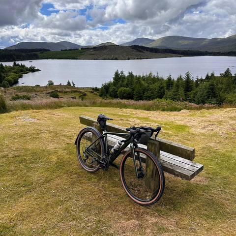Bike propped against wooden bench with loch view in background.